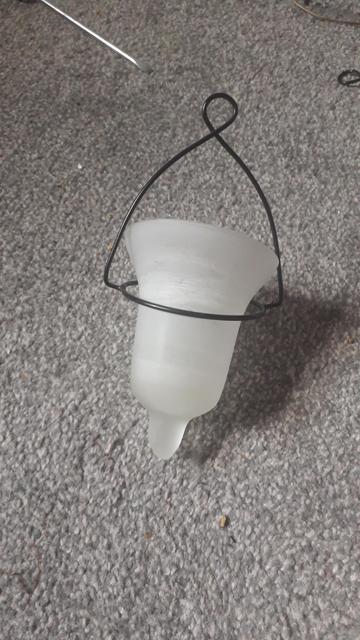 One of the votives sitting on a grey carpet with the wire support around it. You can see the glass it is frosted glass.