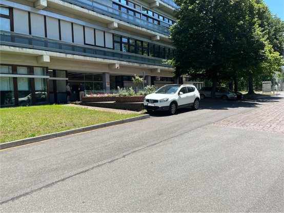 Symbolbild: PKW steht halb auf der Fahrbahn vor dem Eingang eines Gebäudes