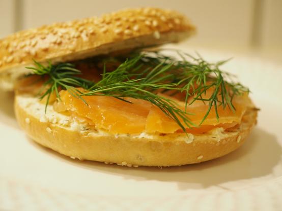 Ein aufgeschnittener und getoasteter Bagel belegt mit Kräuterfrischkäse, Räucherlachs und frischem Dill