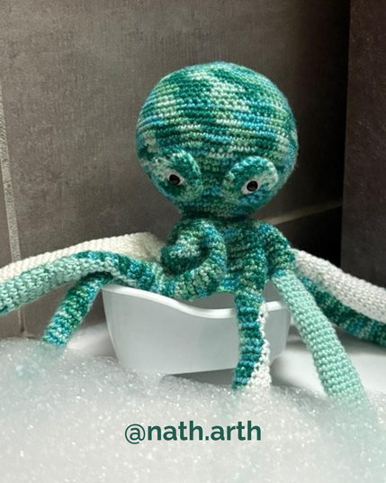 Poulpe au crochet dans les tons bleu-vert mouchetés, installé dans une petite baignoire blanche entourée de mousse, dans une ambiance salle de bain.