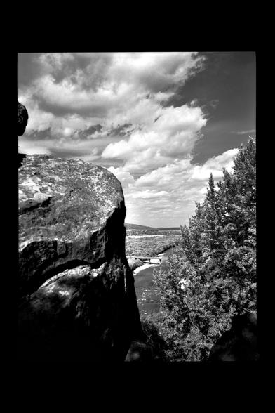 A dramatic view through a rocky cliff toward a winding river, framed by trees and distant hills. The sky is filled with textured clouds, and the high contrast is enhanced by Rollei Infrared 400 film with a red filter. Shot on a Fuji GA645w medium format camera.
