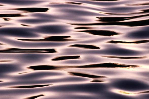 Photograph of shadow spots and blue and purple light reflected off a lake surface at twilight.
