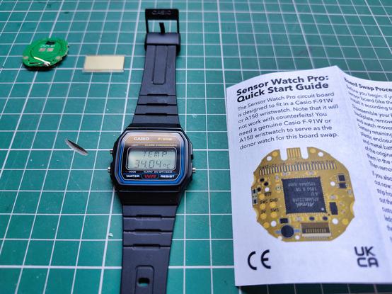 A CASIO F-91W watch is lying on a green cutting mat next to its original PCB and display, as well as the Sensor Watch Pro's instruction leaflet.

The watch's display shows the current temperature as 34.04 degrees Celsius, demonstrating that the watch brain transplant was successful.