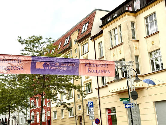Banner mit dem Logo der Kleinstadtakademie, den Kleinstadtkongressdaten, über einer Straße im Zentrum der Kleinstadt Wittenberge, Brandenburg