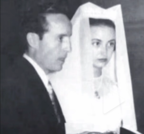 Una pareja en una ceremonia de boda, donde el hombre lleva un traje oscuro y la mujer un vestido de novia con velo.