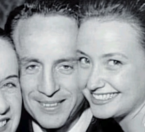 Foto en blanco y negro de tres personas sonriendo juntas, con un enfoque en un hombre en el centro y dos mujeres a cada lado.