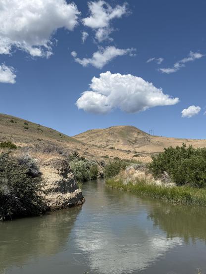 A viewpoint of a curve of a canal, looking up on the far mountain and blue sky. A vividly white cloud hangs above the mountain. The canal is full of water, reflecting the cloud.