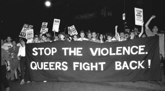 Black and white photo of demonstration, prominently people holding a banner that says "Stop the violence. Queers fight back!"