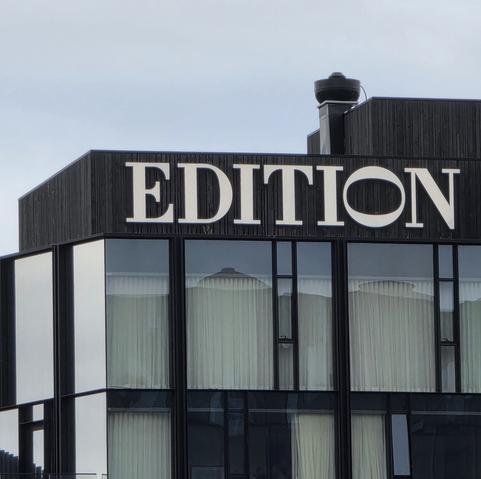 Photograph of a large sign on top of a building in a medium contrast, serif font that says 'EDITION' the O is on its side and is larger proportions to make it's width equal to the hieght of the other letters.