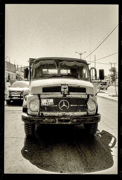 A short bonnet Mercedes truck viewed from the front on the street.