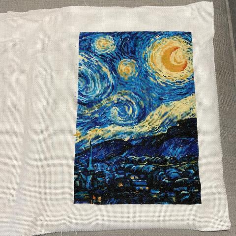 A cross-stitch project in progress, depicting half of Vincent van Gogh's famous painting "The Starry Night." White blank fabric on the left side, the part yet to be finished