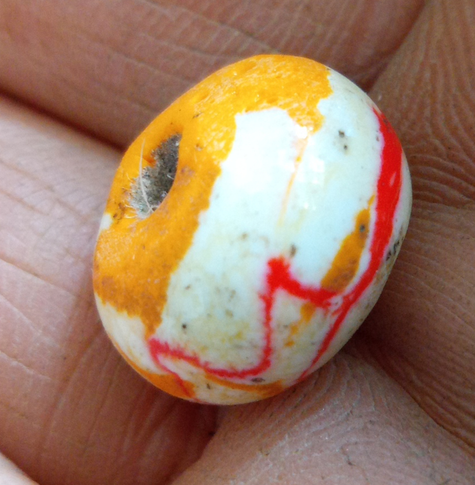 Makro einer gelbweißen Glasperle mit roter Linie auf einer Hand.