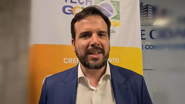 foto com homem jovem responsável pela Anatel em frente ao banner de um evento