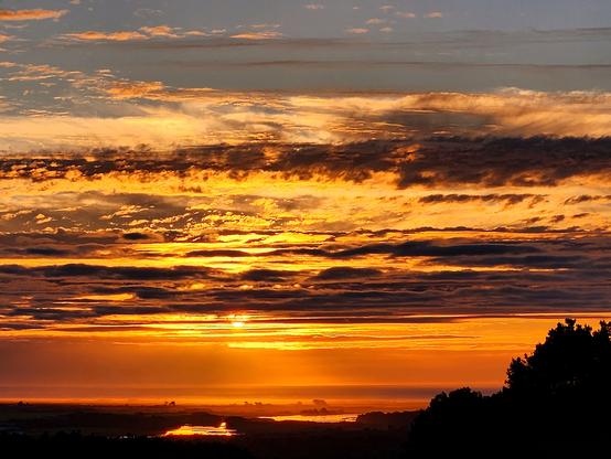 Clouds layered orange and dark lines in the sky at sunset. The orange is reflected on the river.