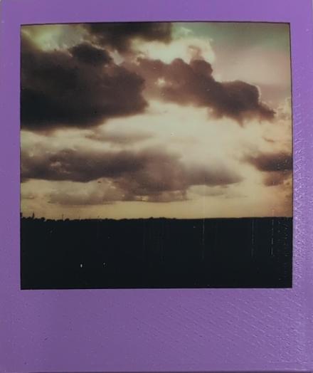 Photo of a Polaroid picture, landscape with brown blue tinge showing sunlight poking through the cloud cover