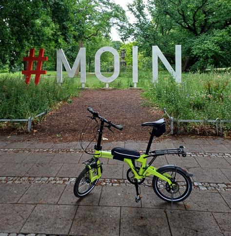 Faltrad vor einer Skulptur (Schriftzug #MOIN)