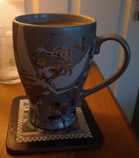 Silver mug of tea on a bedside cabinet, with a picture of Tinkerbell