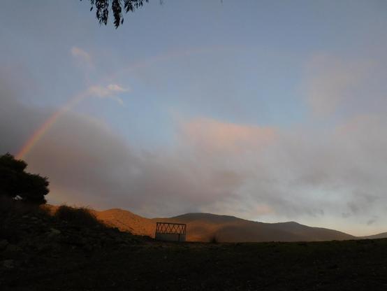 Rainbow extending over the valley, with hay feeder silhouetted on the ridge in the foreground
