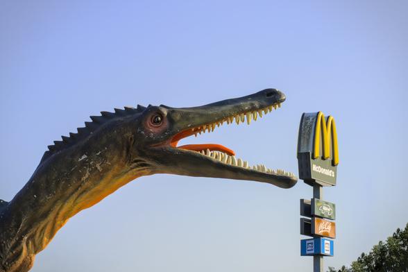 Ein (künstlicher) Dinosaurier, der ein McDonald's Schild zu fressen scheint
