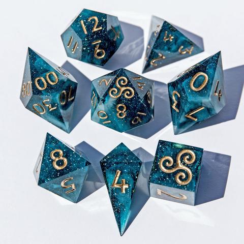 Ein Würfelset in Petrol mit weißen Swirls im inneren und Nummern in Goldbronze. Das Set besteht aus einem D4-Shard, einer D4-Pyramid, D6, D8, D10, D100, D12 und D20. Das Set liegt auf weißem Untergrund mit der höchsten Seite nach oben. Die Würfel sind im Bild um den D20 angeordnet.