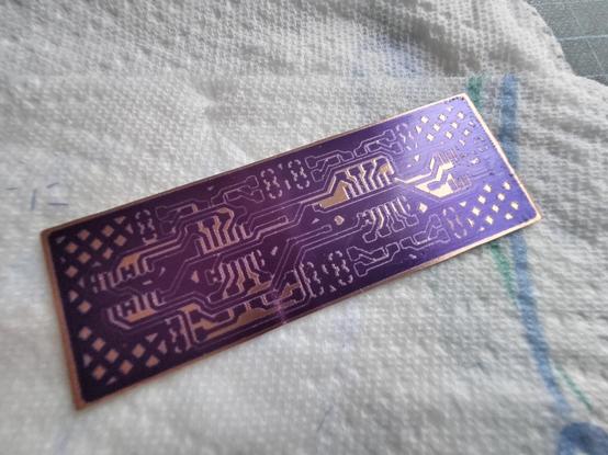 Photo of a tiny PCB with developed photoresist. It looks… ok? Probably slightly overdeveloped in an attempted to get the fine features to fully clear.