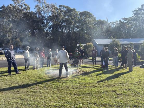 People gathered around a fire tended by a ranger from an Aboriginal Corporation