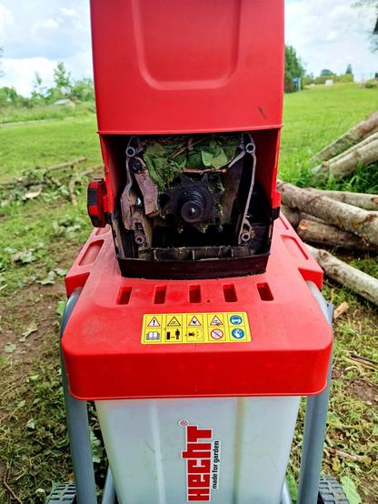 A cheap electric branch shredder that has been upgraded with some custom made steel parts. The front cover is removed, exposing the crushing wheel, which is jammed with a bunch of oak leaves from the top.