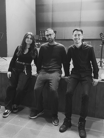 Foto a bordo palco. Al centro il docente, Nicola Monopoli, affiancato dai suoi due allievi, Simona Dichio ed Eugenio Granieri, al termine di un’esecuzione di brani per cajón ed elettronica. L’atmosfera è rilassata e amichevole, in bianco e nero.