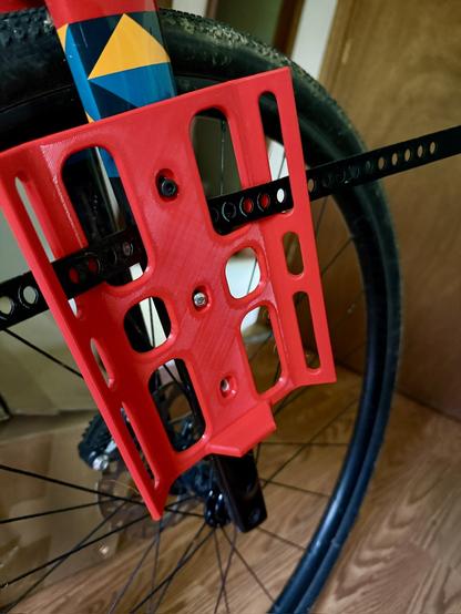 A 3d printed bike front fork cage partially mounted (missing a screw) and showing a TPU strap wound through the holes