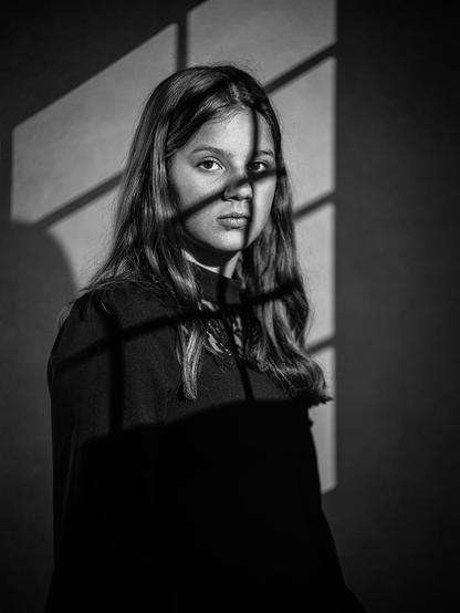 Studio portrait of a 12-year-old girl onto whom a window light with a window cross was projected by flash.