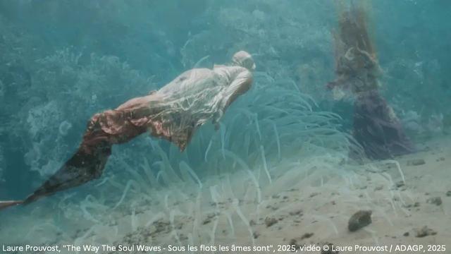 Capture d’écran de la vidéo de Laure Prouvost, "The Way The Soul Waves - Sous les flots les âmes sont", 2025, vidéo © Laure Prouvost / ADAGP, 2025
Deux figures vêtues de longues robes nagent sous l’eau, dans une mer bleue pâle, près du fond, où l’on voit des algues.