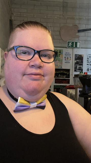 A selfie of me. I’m wearing a bowtie in the nonbinary flag colors