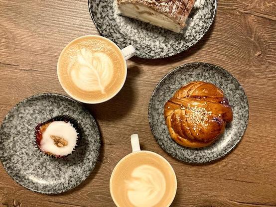 Overhead shot of two coffees, a pastry, a bun, and a cupcake on grey plates.
