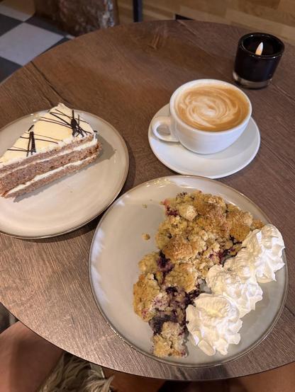 A table setting with a slice of layered cake, a cup of coffee, and a crumble dessert with whipped cream. A small candle is also on the table.