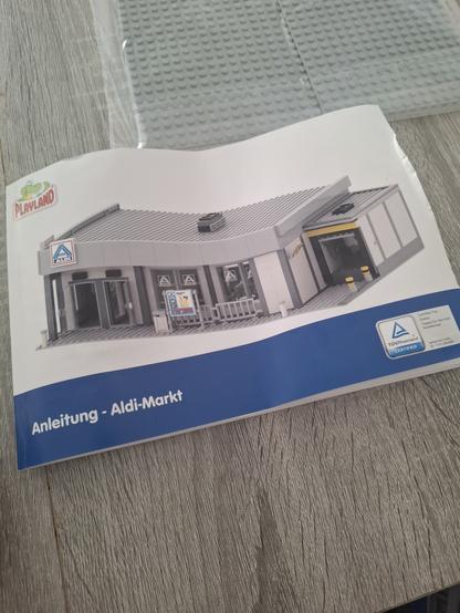 Anleitung Cover des Klemmbausteinsets von Playland, darauf zu sehen ein Grauer Aldi Nord Markt