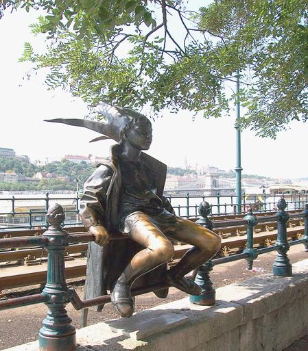 "Kleine Prinzessin" ist eine Skulptur, die auf einem Geländer an der Budapester Donaupromenade sitzt. Inspiriert wurde der Bildhauer László Marton von seiner kleinen Tochter, die sich als Kind oft als Prinzessin verkleidete. Er bastelte ihr eine Krone aus Zeitungspapier und sie erfand einen Bademantel als Robe.
"Little Princess" is a sculpture that sits on a railing on Budapest's Danube promenade. The sculptor László Marton was inspired by his young daughter, who often dressed up as a princess as a child. He made her a crown out of newspaper and she invented a bathrobe as a robe.