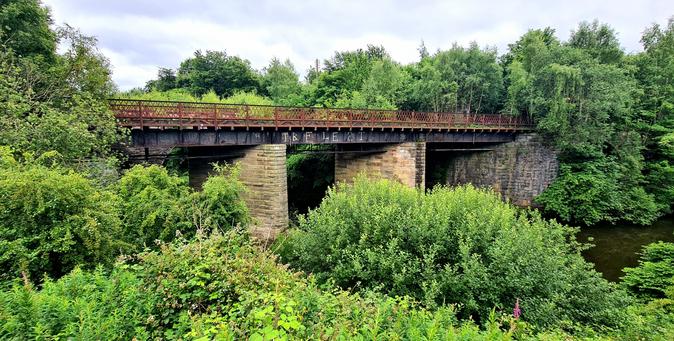 An abandoned railway bridge over the heavily overgrown banks of a small river in Glasgow.
