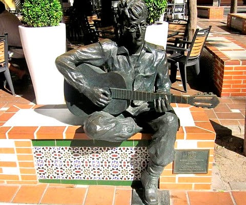 Statue of John Lennon, seated and playing a guitar, in a square in downtown Almería, Spain, where he wrote "Strawberry Fields Forever" inspired by the sweeping open fields of red flowers surrounding the Andalusian city.