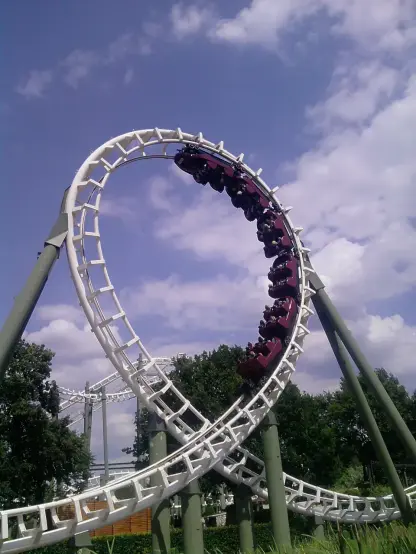 The image shows a roller coaster, specifically an inverted coaster, featuring a loop where riders are suspended upside down. The structure is primarily white and green, with a blue sky and clouds in the background, suggesting it is taken in an amusement park on a sunny day. The design emphasizes thrills and excitement for those riding it.

Image Credits: Wikimedia / YanCoasterman / CC0