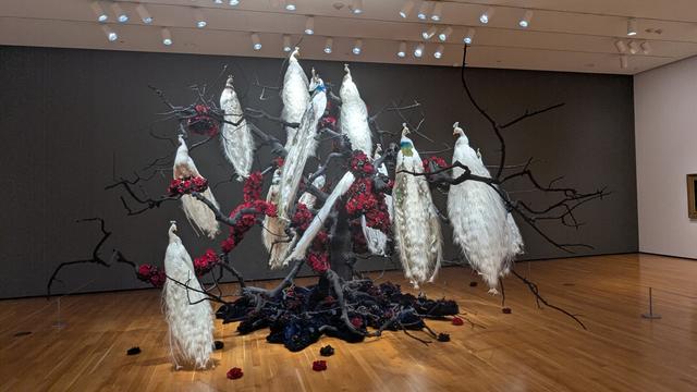 A sculpture installation with white peacocks sitting on black branches.