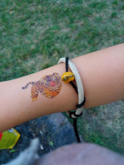 Ein Kinderarm mit Tigertattoo und Armreif mit gelbgrüner Glasperle.