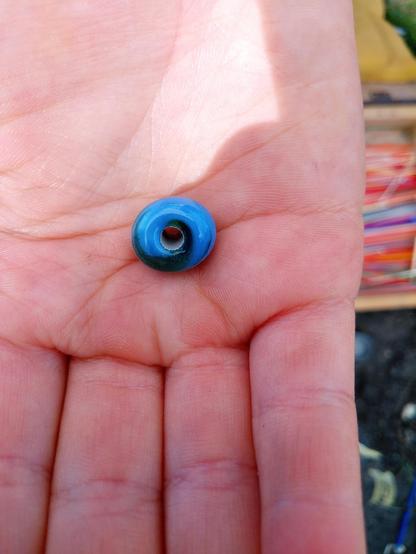 Eine Kinderhand hält eine grünblaue Glasperle.