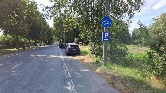 Benutzungspflichtiger Radweg neben einer Straße - von Autos zugeparkt. Unter dem Radweg-Schild hängt ein blaues Parkplatz-Schild mit einem Pfeil nach links.
