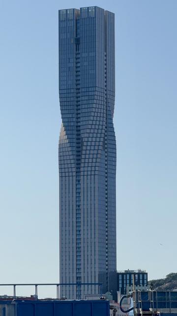 A tall, modern skyscraper with a unique, wave-like design. The building features a glass façade and is set against a clear blue sky.