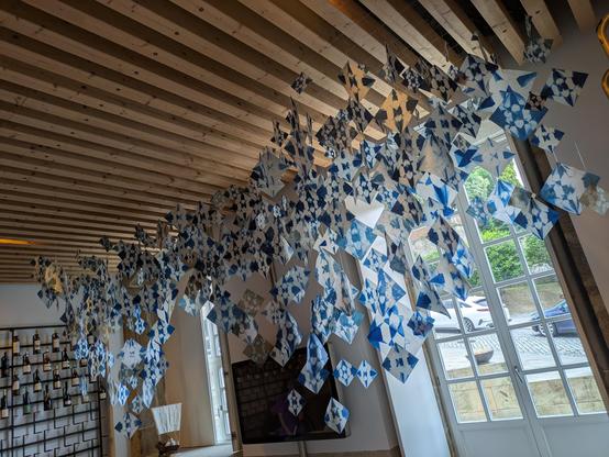 Updated version of the previous image - installation of several hundred origami cranes as cyanotype images, finally done, in a wine tasting room with wooden beam ceiling and windows behind the hanging