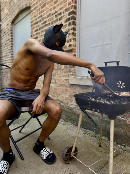 Pup Nash serves as the grill master, flipping a burger while sitting on a folding chair