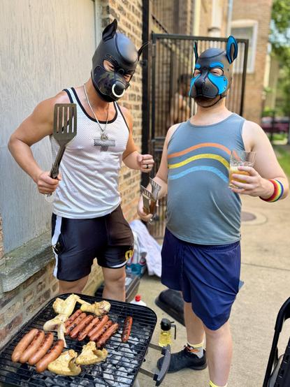 Two pups stand behind a small charcoal grill laden with sizzling hot dogs and chicken wings. The pup on the left is muscular, wearing a black/camo neoprene puppy hood with a white nose ring, a white mesh tank top, and black shorts. He flexes while holding a large spatula. His companion wears a blue-and-black puppy hood, a grey tank top with rainbow stripes, and a rainbow wristband, holding a glass of beer and a pair of tongs