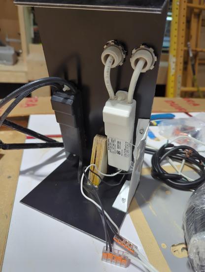 Black and white metal bent and riveted with wood block and black and white plastic transformers mounted to it. Ceramic bushings come through with the high voltage wires. An orange WAGO connector connects primary wires.