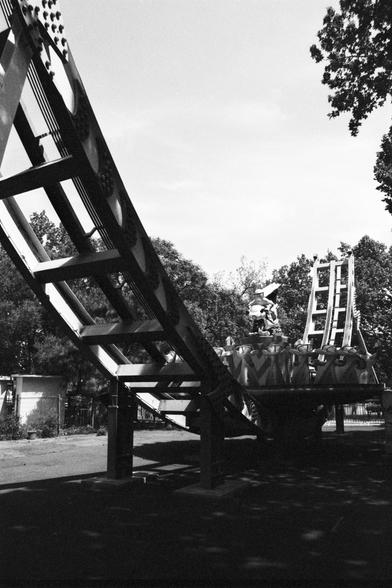 Lucky Lucky SHD 400 (FF)

English alt text:
A black and white photo of a roller coaster in an amusement park, featuring a curved track and ride vehicles. Trees and a small building are visible in the background.

中文替代文本（Chinese alt text）：
一张游乐园过山车的黑白照片，展示了弯曲的轨道和车厢。背景中有树木和一座小建筑。