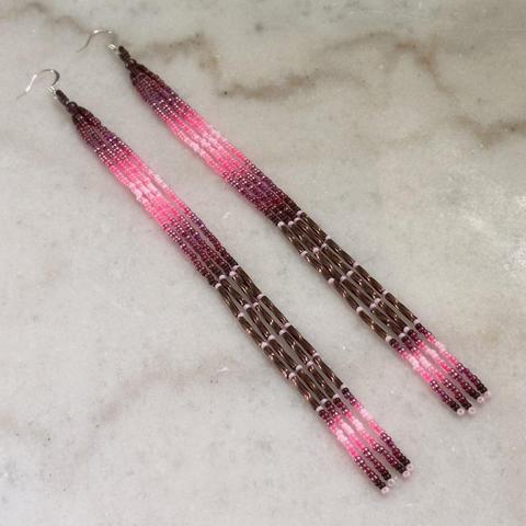A pair of long beaded dangle earrings in shades of pink and brown against a white marble background